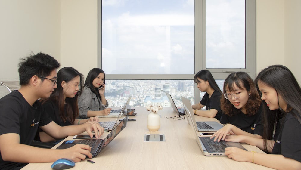 six people sitting at table using laptop computers