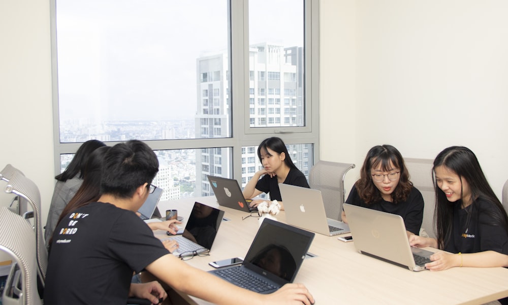 six people sitting at table using laptop computer