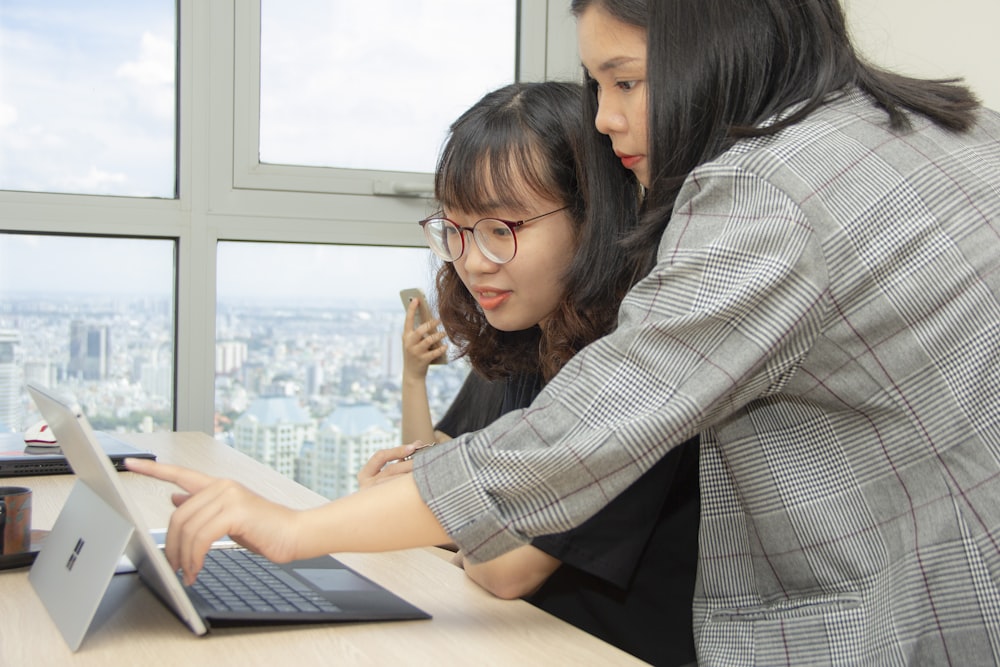 woman standing behind sitting woman in front of laptop computer