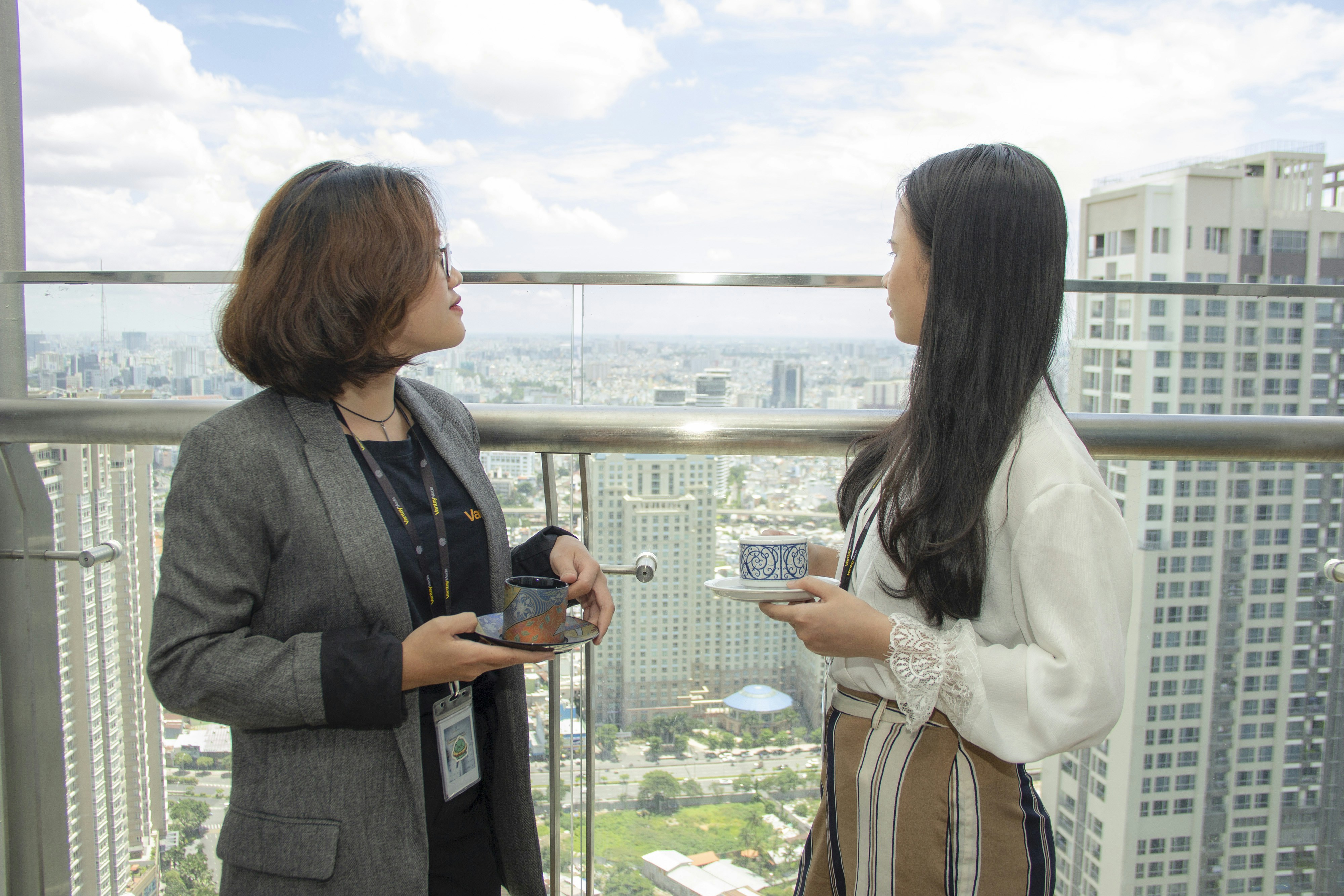 two women having coffee break by the glass window overlooking the city