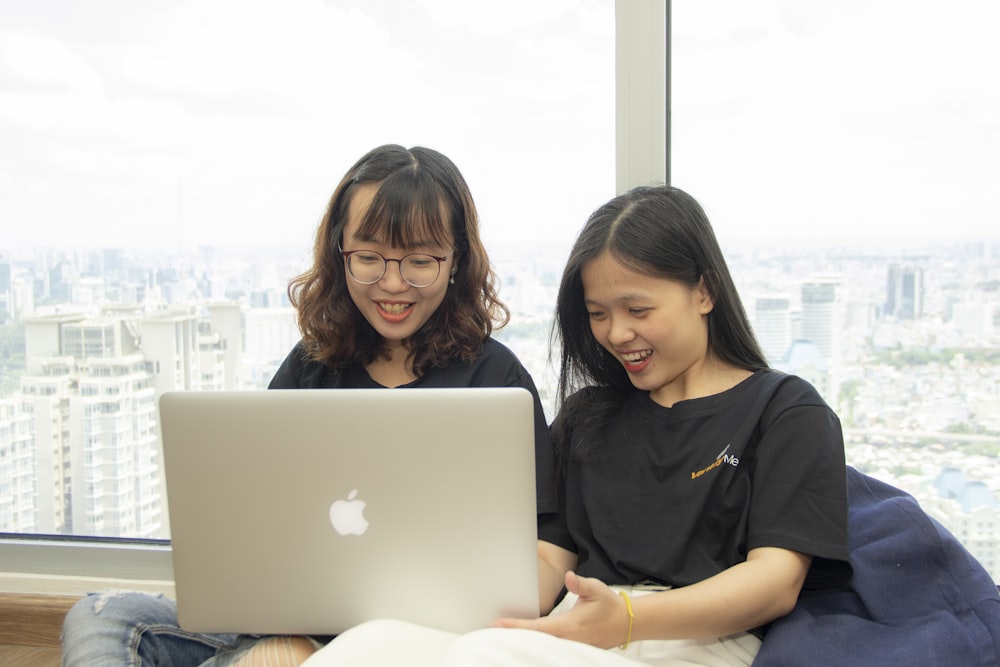 two women sitting beside silver MacBook close-up photography