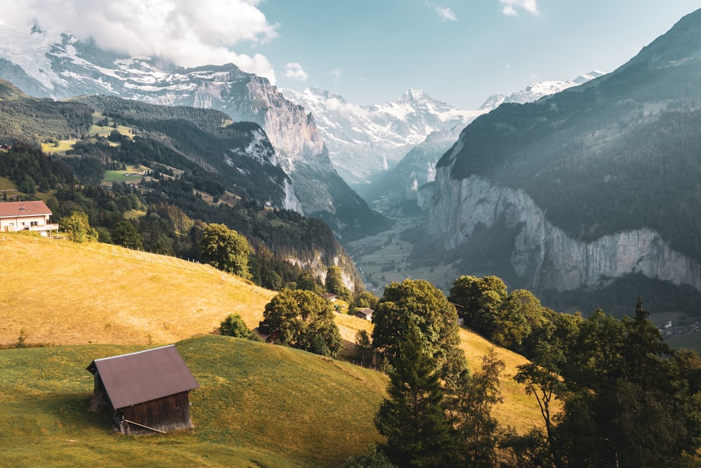 brown house beside green trees near mountains at daytime