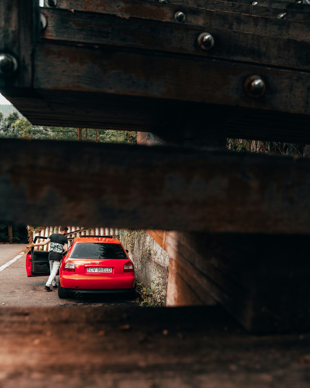 person going in red hatchback parked beside wall