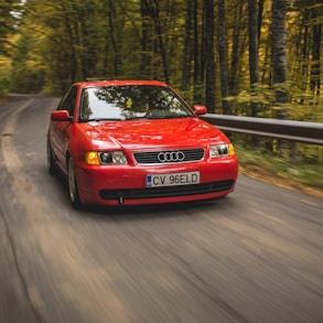 red Audi sedan passing on road between trees during daytime