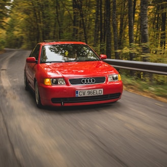 red Audi sedan passing on road between trees during daytime