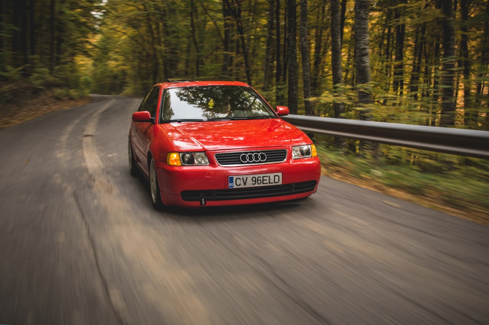 Audi sedán rojo que pasa por la carretera entre árboles durante el día
