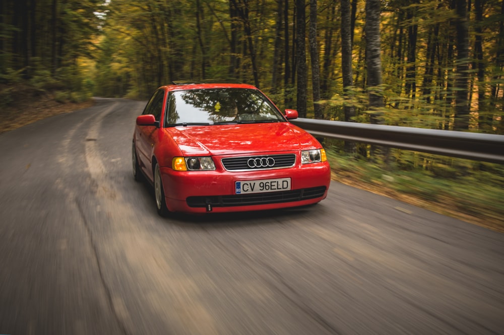 red Audi sedan passing on road between trees during daytime