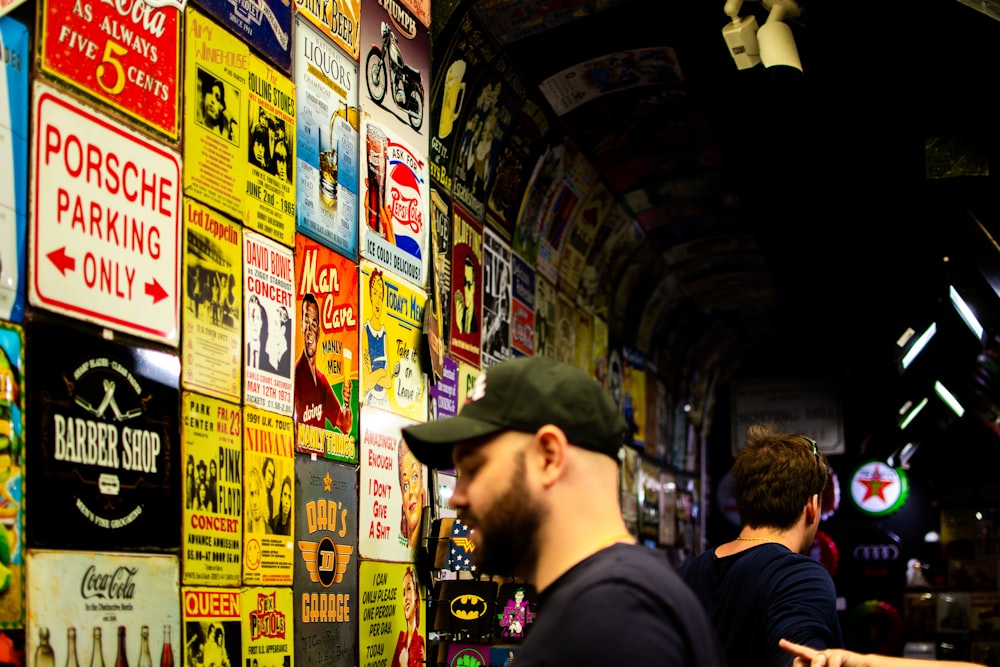 man wearing black shirt and cap standing in front of posters