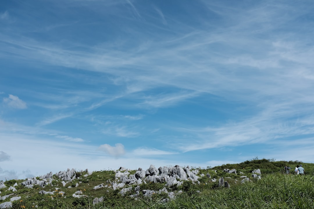 green hill with rocks under white clouds and blue sky during daytime