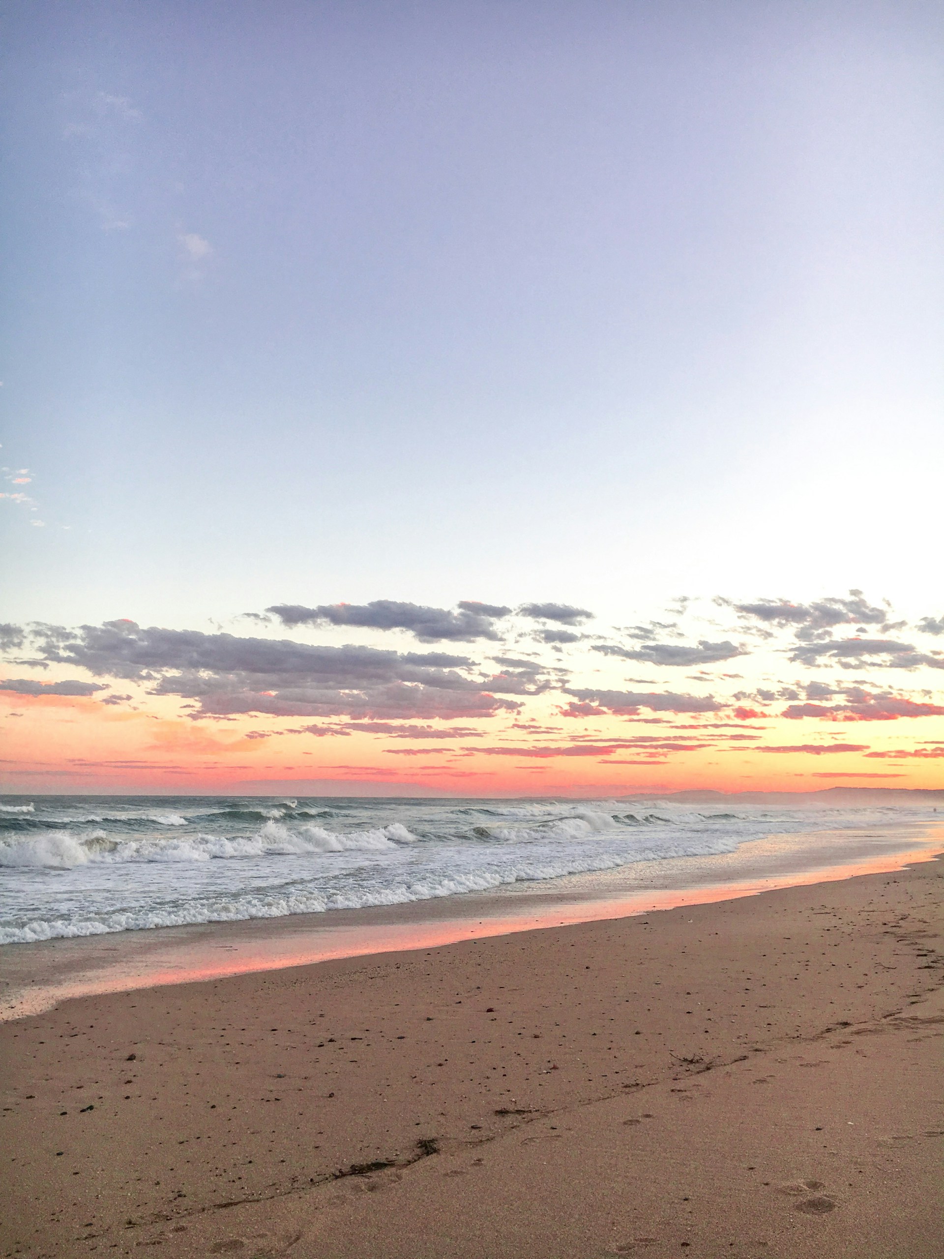A tranquil beach at sunset with soft waves and warm colors reflecting on the water.
