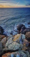 A rugged coastline with waves crashing against jagged rocks at sunset.
