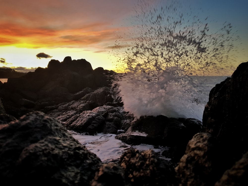rock formations with sea wave under orange and yellow skies