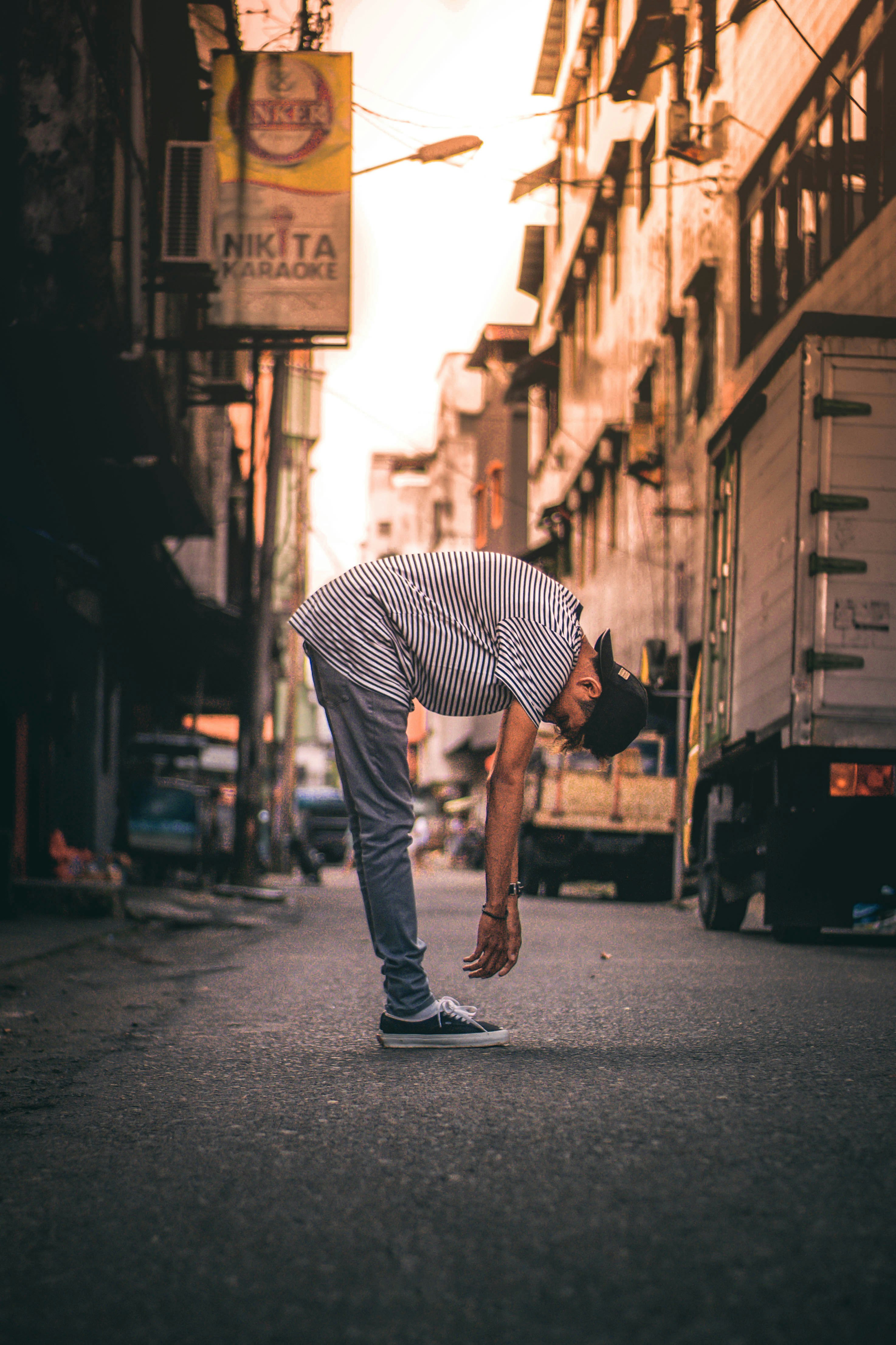 man wearing white and black striped shirt bending near road beside buildings