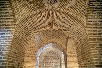 A series of intricately designed brick arches form a structure with geometric patterns. The arches are constructed with reddish-brown bricks, providing a sense of depth and perspective.