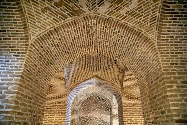 A series of intricately designed brick arches form a structure with geometric patterns. The arches are constructed with reddish-brown bricks, providing a sense of depth and perspective.