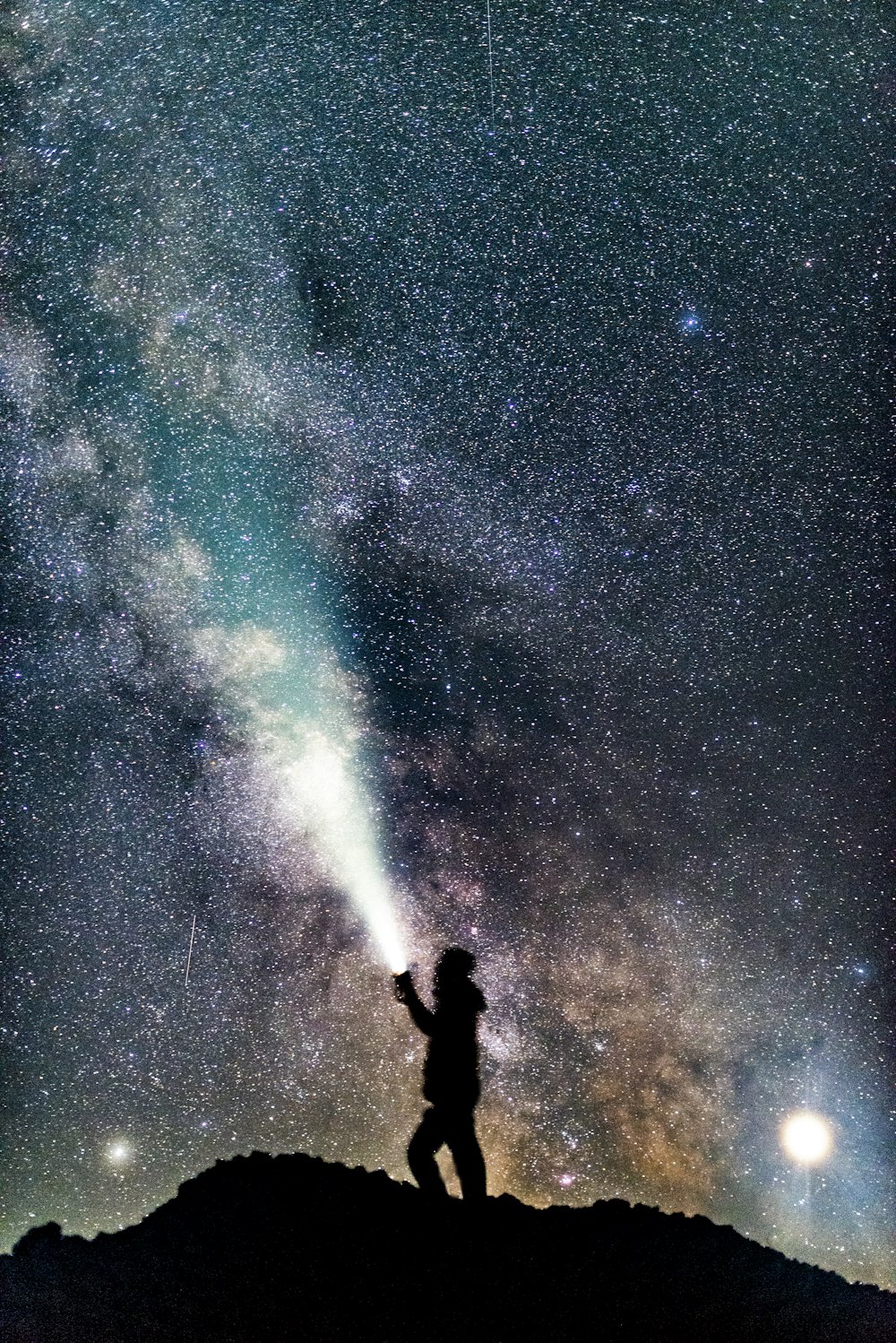 uma pessoa em pé no topo de uma colina sob um céu cheio de estrelas