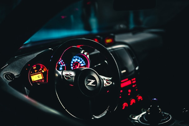 A car interior highlighting a sleek steering wheel with a 'Z' logo and an illuminated dashboard displaying vibrant red and blue lights. The design gives a modern and dynamic feel, with the gearshift visible in the foreground.