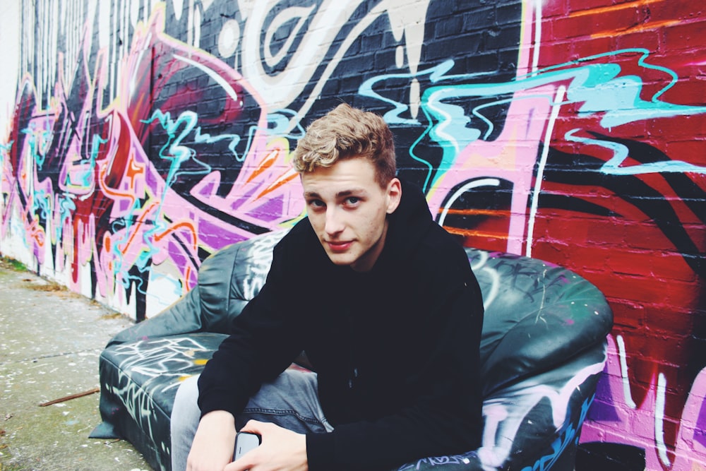 a man sitting on a couch in front of a wall with graffiti