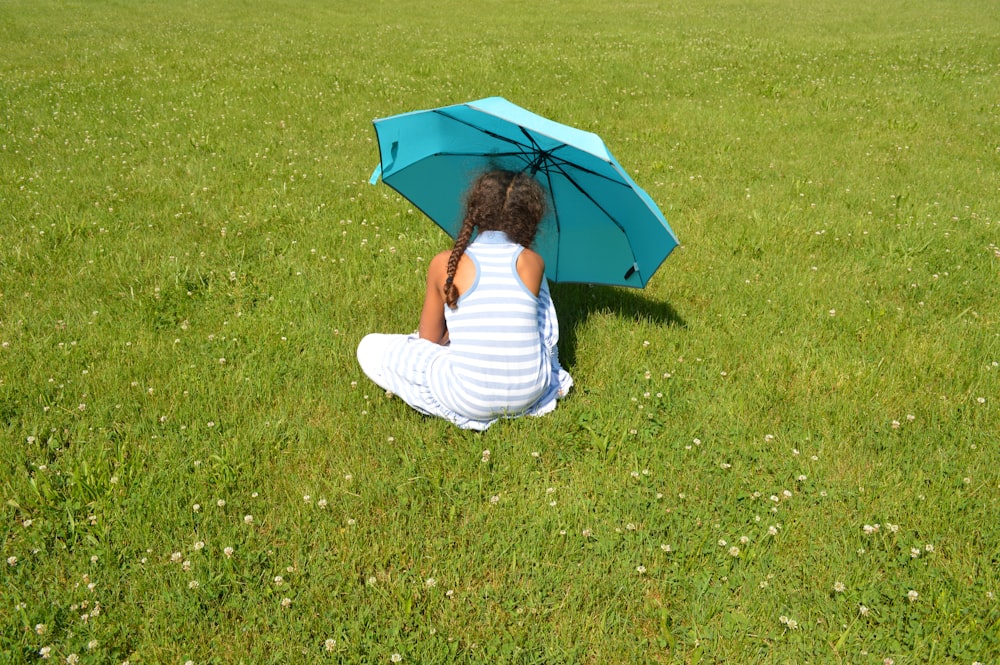 girl sitting on green grass field under umbrella
