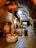 A dimly lit underground cellar featuring a large wooden wine press. The stone flooring and arched brick ceiling add a rustic feel to the setting. Various winemaking equipment, including a metal barrel and a red basket press, are visible.