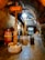A dimly lit underground cellar featuring a large wooden wine press. The stone flooring and arched brick ceiling add a rustic feel to the setting. Various winemaking equipment, including a metal barrel and a red basket press, are visible.
