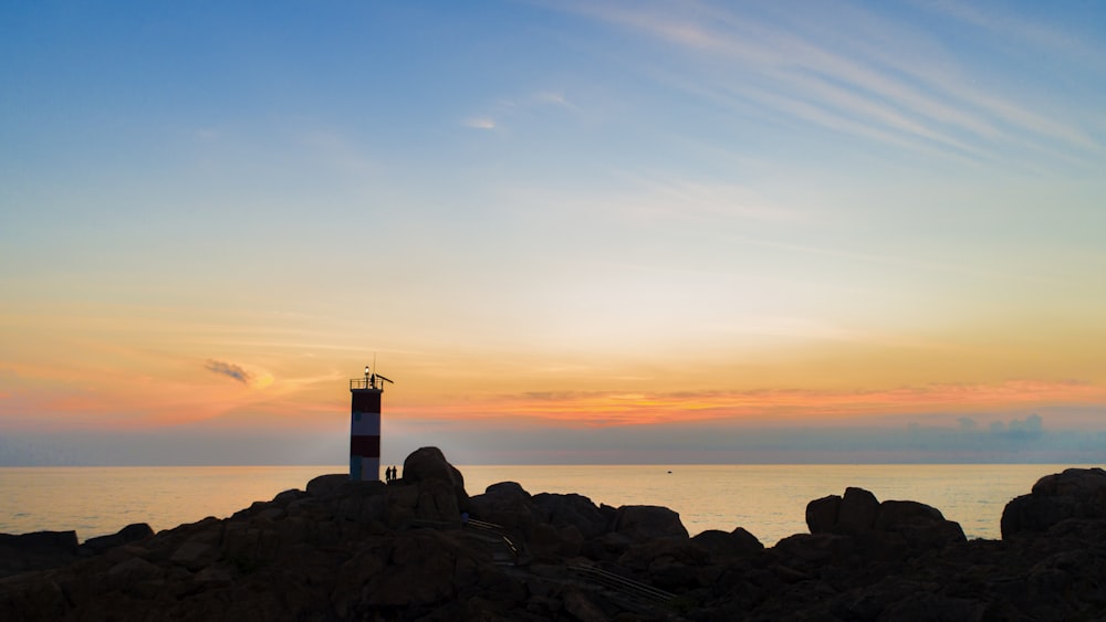 silhouette photography of lighthouse by the sea during golden hour