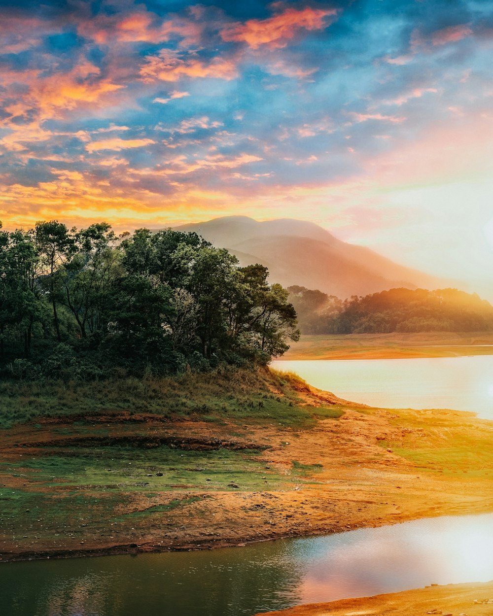 green field viewing lake under orange and blue skies