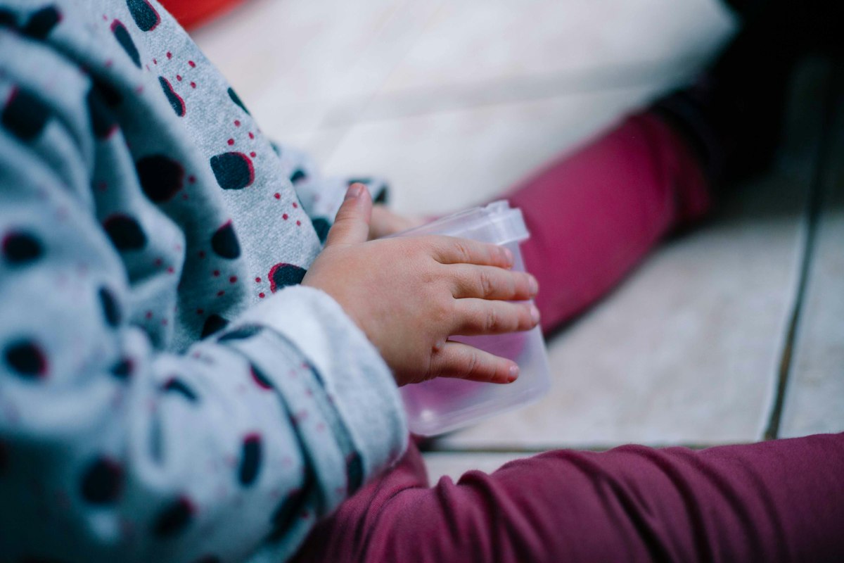 A child's hands holding a small clear snack container