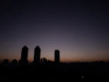 A minimalist city skyline silhouette against a pale blue sky just before dawn.