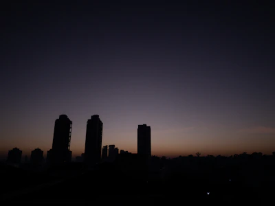 A minimalist city skyline silhouette against a pale blue sky just before dawn.