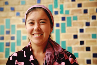 Aya El Jazzar smiling warmly while speaking in front of a camera, with a cozy, inviting background.