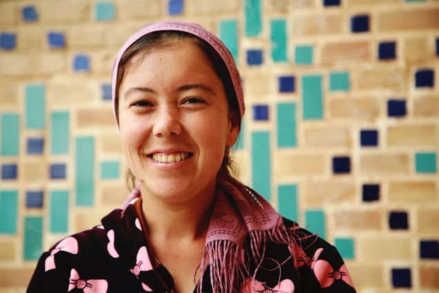 A warm portrait of Hamida Osmanova smiling in front of an Italian cityscape with terracotta rooftops.