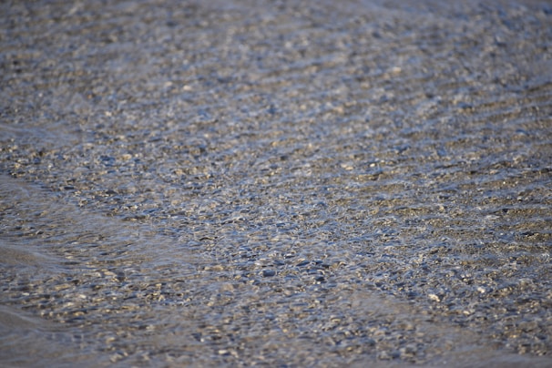 Close-up of shimmering water reflecting sunlight, with a hint of a chic swimsuit edge visible.