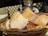 A close-up view of a basket filled with crispy, golden-brown bread pieces. The bread is beautifully textured, with a slightly crispy crust and a soft interior. The basket is wicker, providing a rustic appearance, and is placed on an outdoor table with a blurred background, suggesting a café setting.