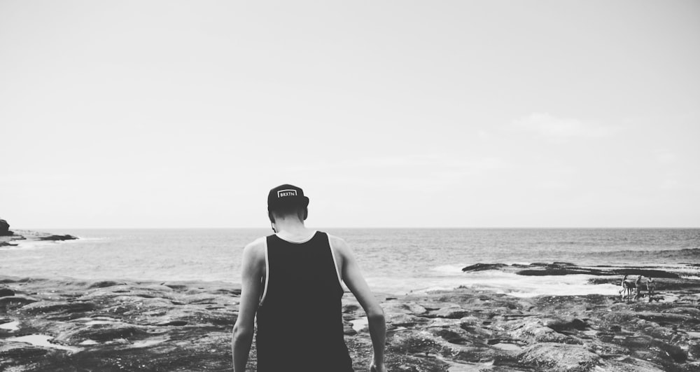 해안을 걷는 남자의 회색조 사진