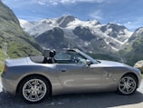 A sleek car parked on a scenic road with mountains.