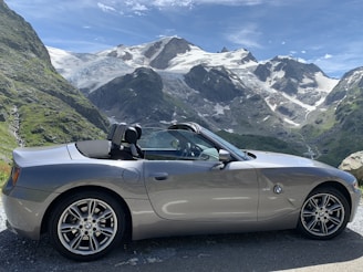 A sleek rental car parked on a scenic road with mountains in the background.