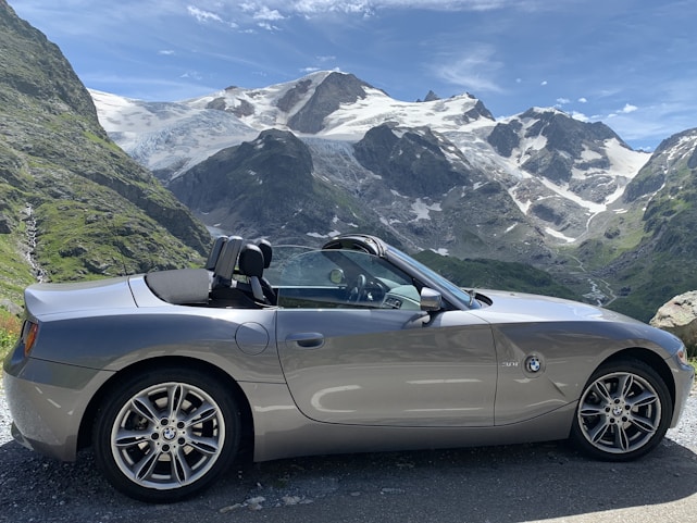 A sleek rental car parked on a scenic road with mountains in the background.