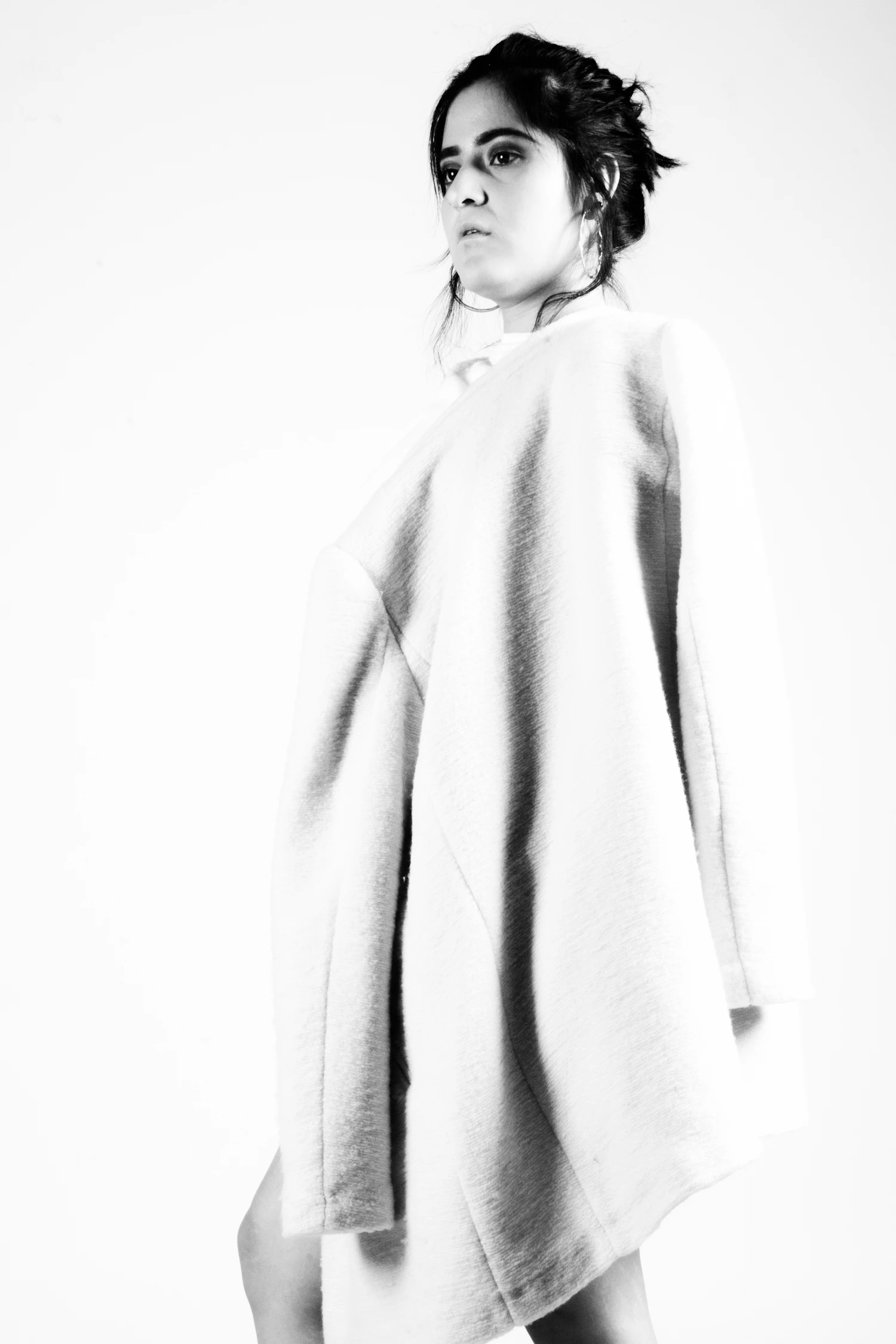 A heavy white wool coat worn open, photographed against a pale wall