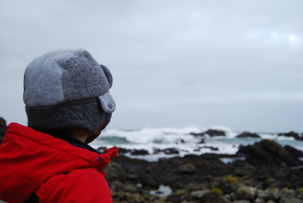 person wearing red hooded top facing the field of rocks and ocean