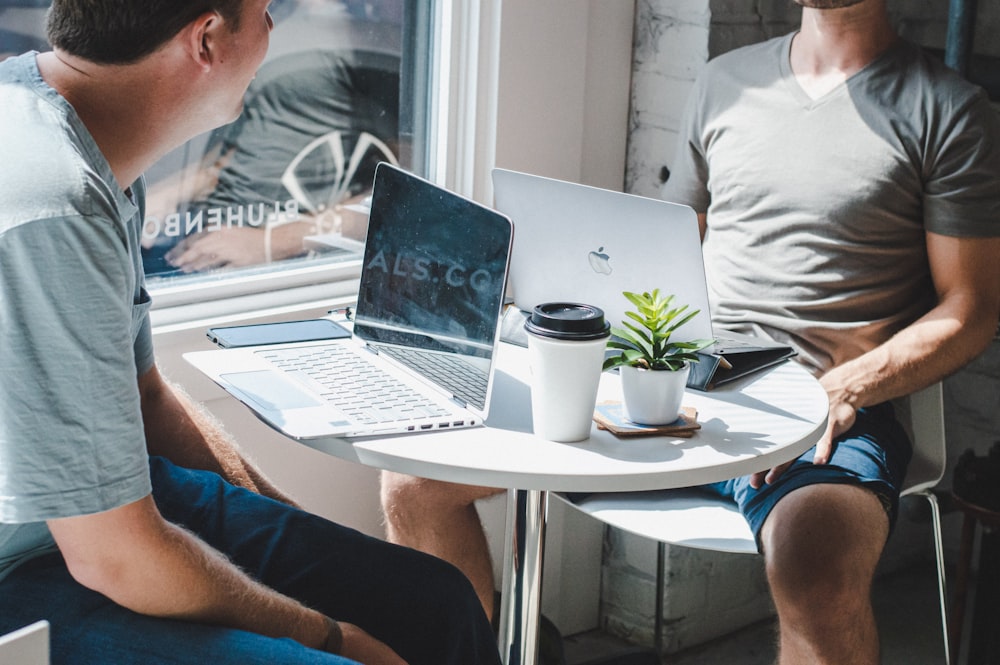 two gray laptop on table infront of two men