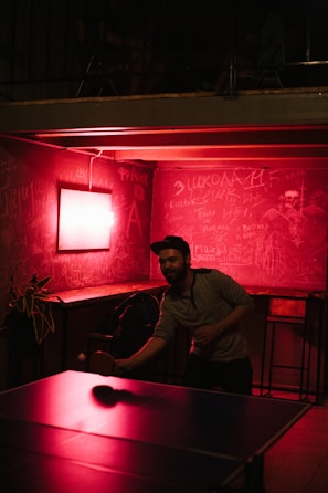 A group of players intensely focused during a fast-paced table tennis rally under purple lighting.