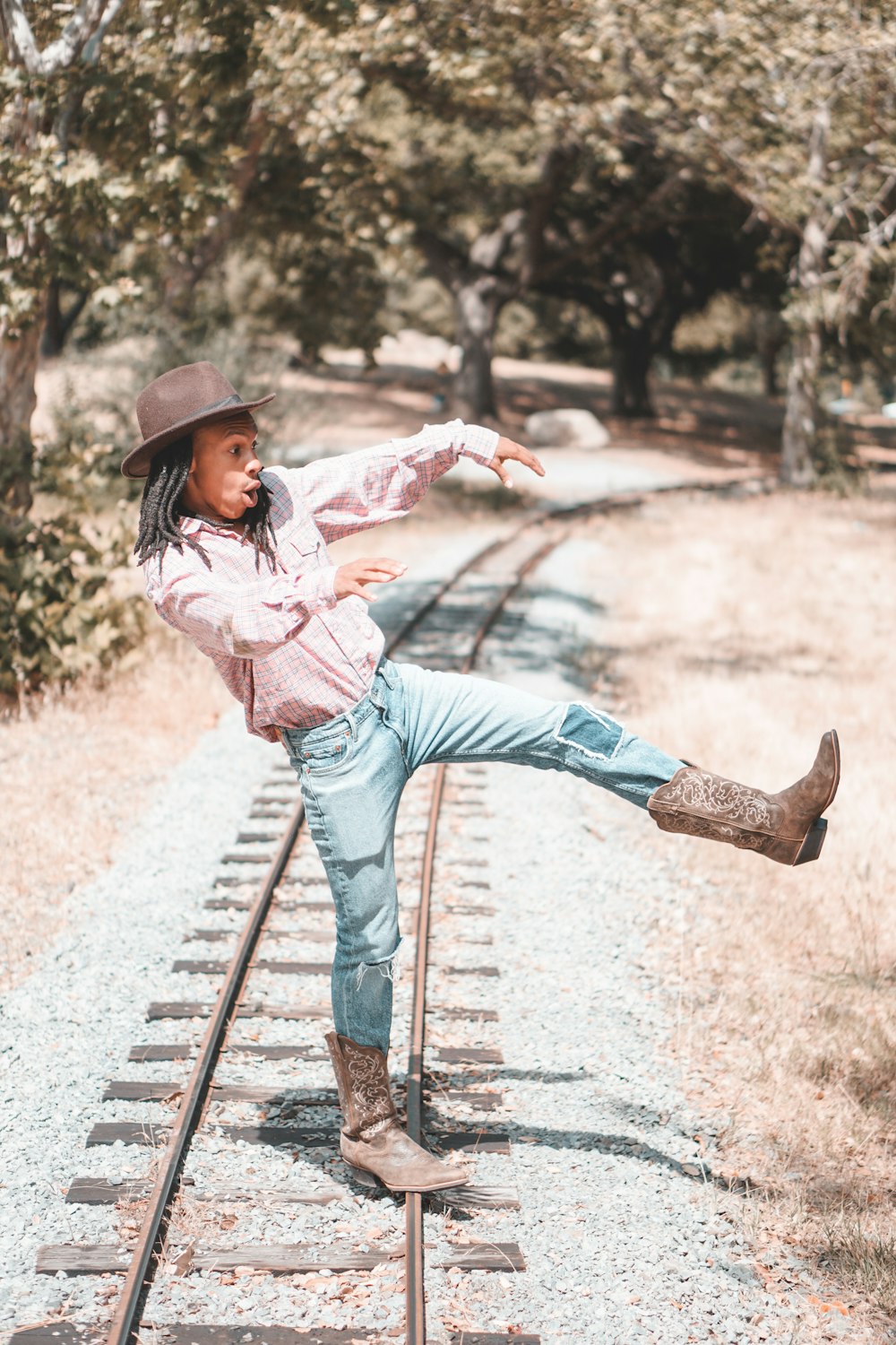 man wearing pink collared button-up long-sleeved shirt standing and raising left foot near train railway