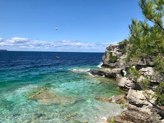 person riding boat near cliff on sea in Bruce Peninsula National Park Canada