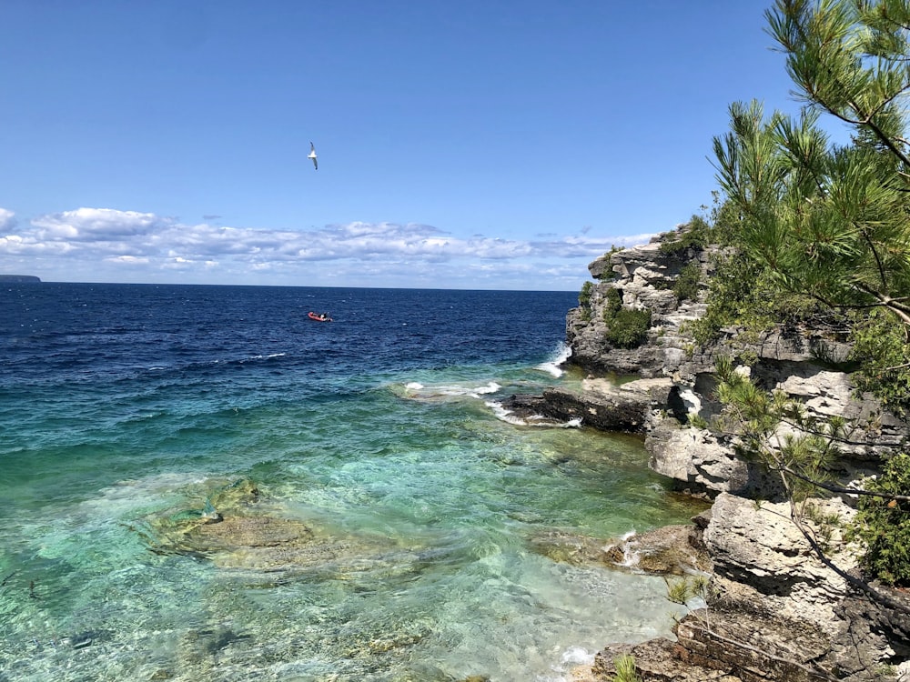 person riding boat near cliff on sea