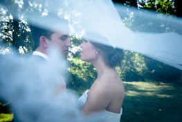 Elegant couple sharing a quiet moment, framed by pale green foliage and soft beige drapery.