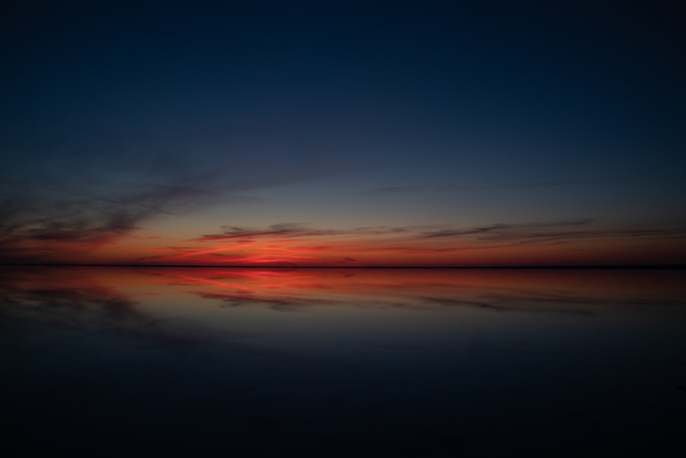 the sun is setting over a calm lake