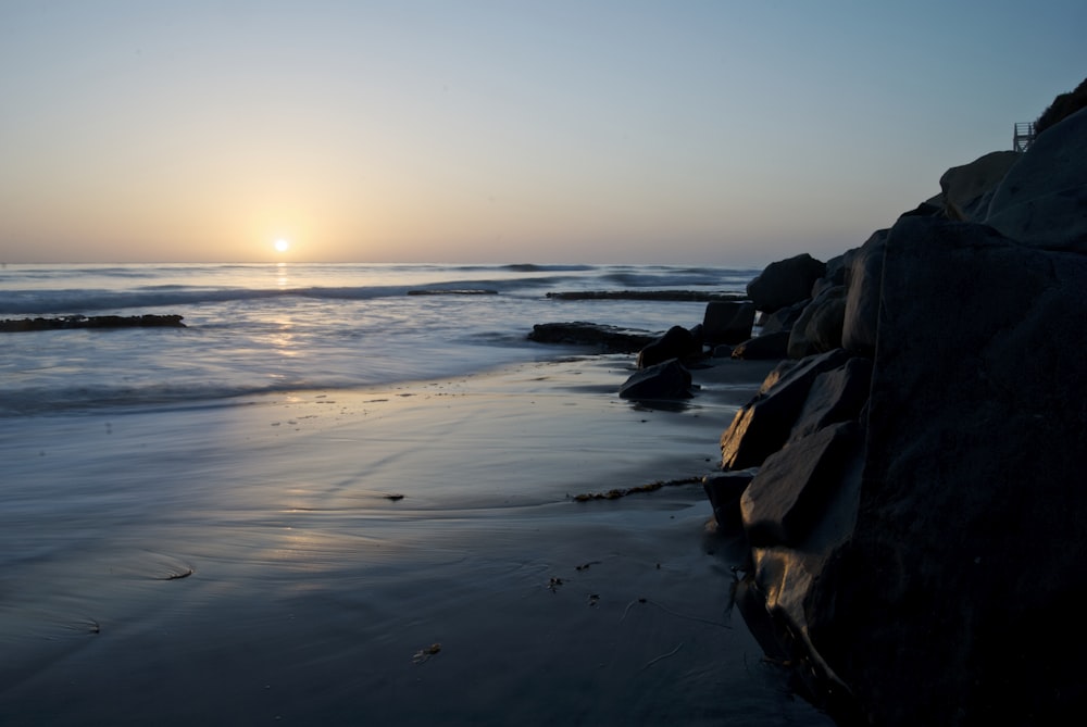 the sun is setting over the water at the beach