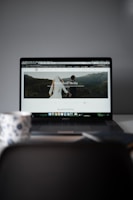 A laptop displaying a website with a large header image of a couple holding hands and looking towards a mountainous landscape. Text on the screen reads 'Randelhoff Media.' In the foreground, a blurred coffee cup with a floral pattern is visible.