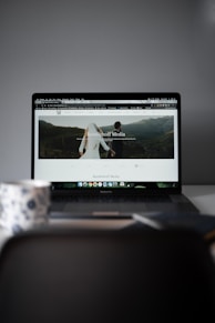 A laptop displaying a website with a large header image of a couple holding hands and looking towards a mountainous landscape. Text on the screen reads 'Randelhoff Media.' In the foreground, a blurred coffee cup with a floral pattern is visible.